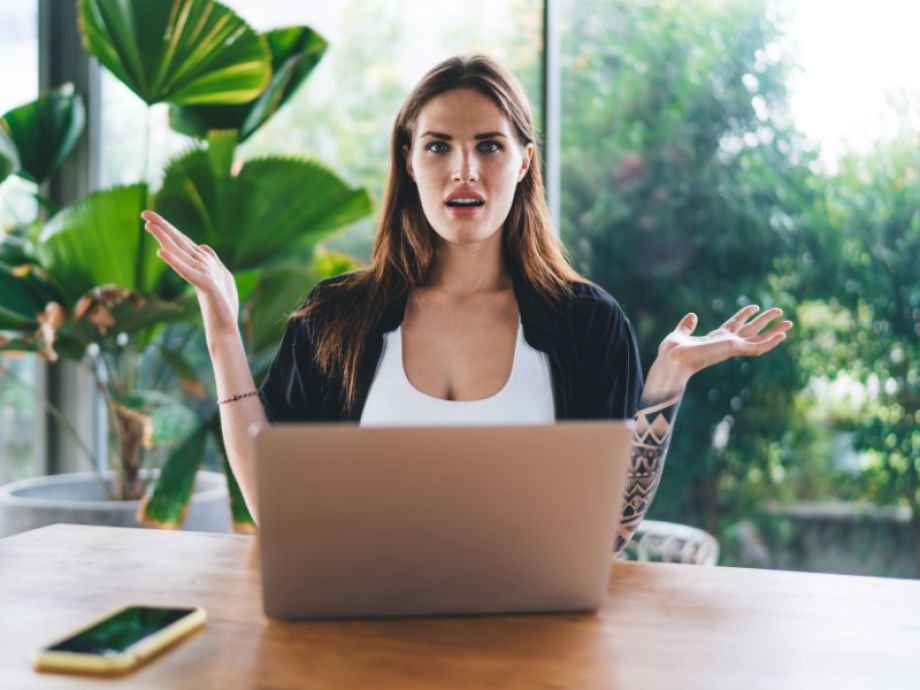 Twijfelende vrouwelijke ondernemer achter laptop, denkend over de keuze tussen een VA of businesscoach.