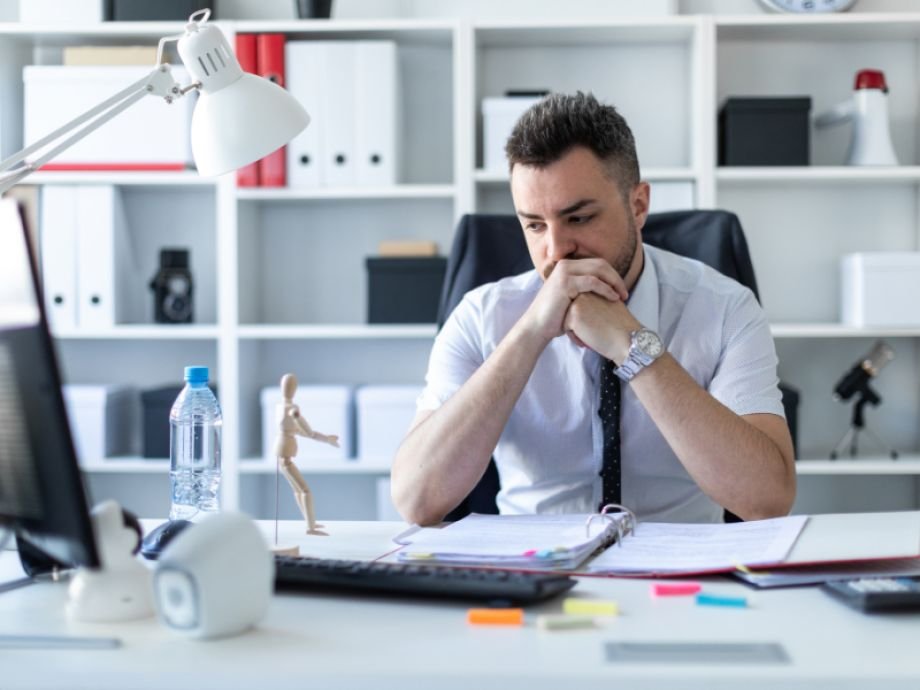 Ondernemer zittend aan bureau, hoofd in handen, uitdrukking van faalangst en innerlijke worsteling.