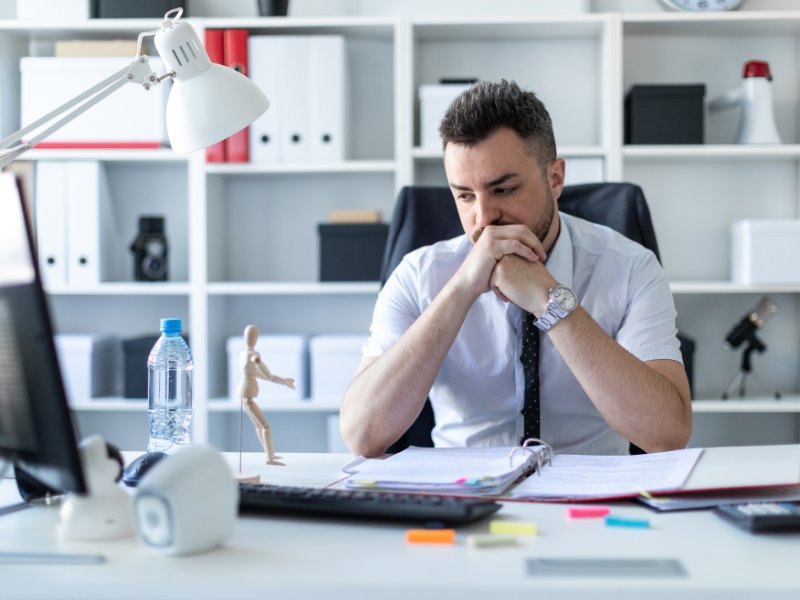 Ondernemer zittend aan bureau, hoofd in handen, uitdrukking van faalangst en innerlijke worsteling.